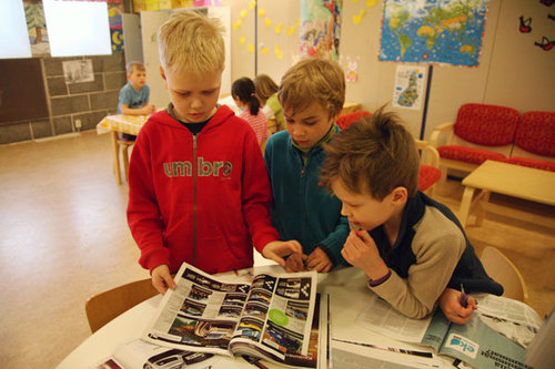 Tre barn som läser i tidningar tillsammans.