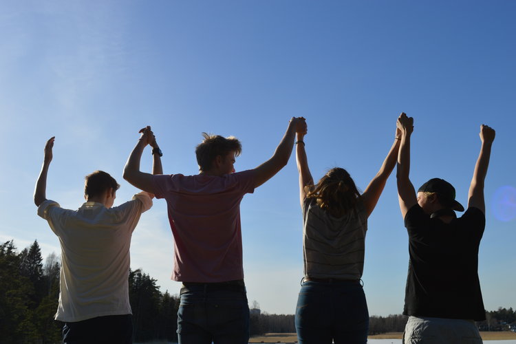 Ungdomar tillsammans med lyfta händer mot blå himmel