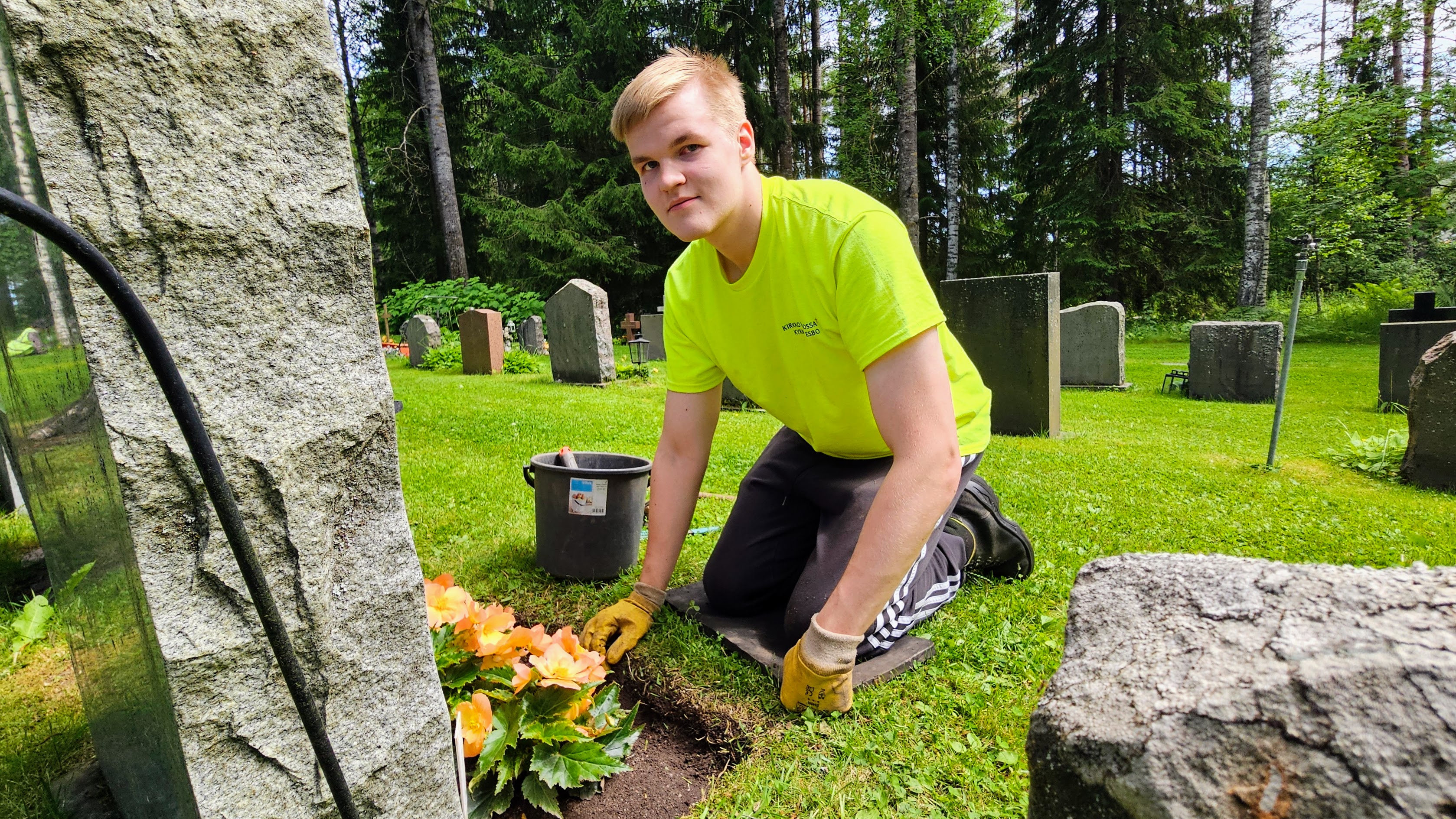 En ung man i gul skjorta på huk framför en gravvård.