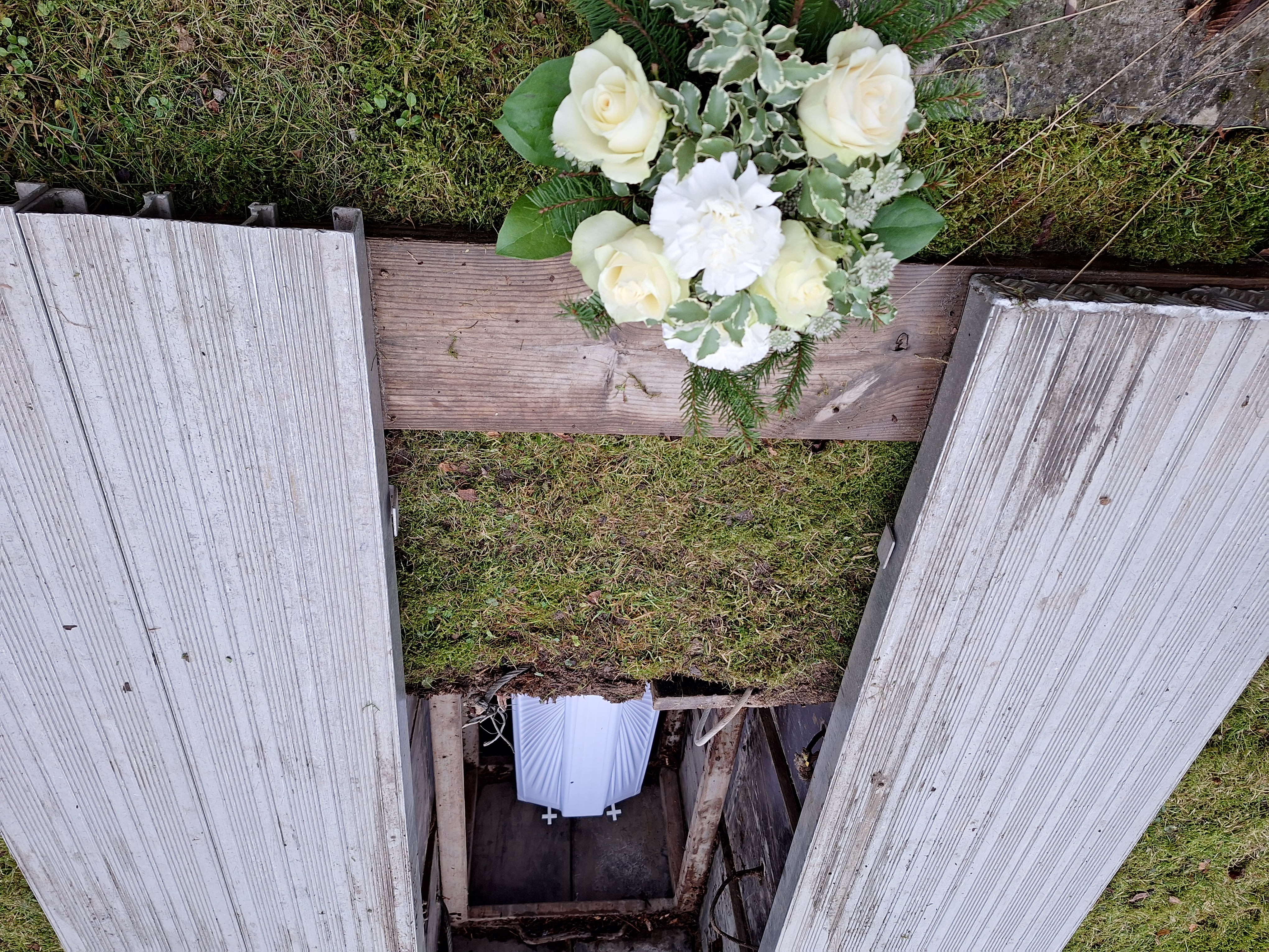 En vitdraperad kista i en öppen grav och en blombukett med vita blommor.