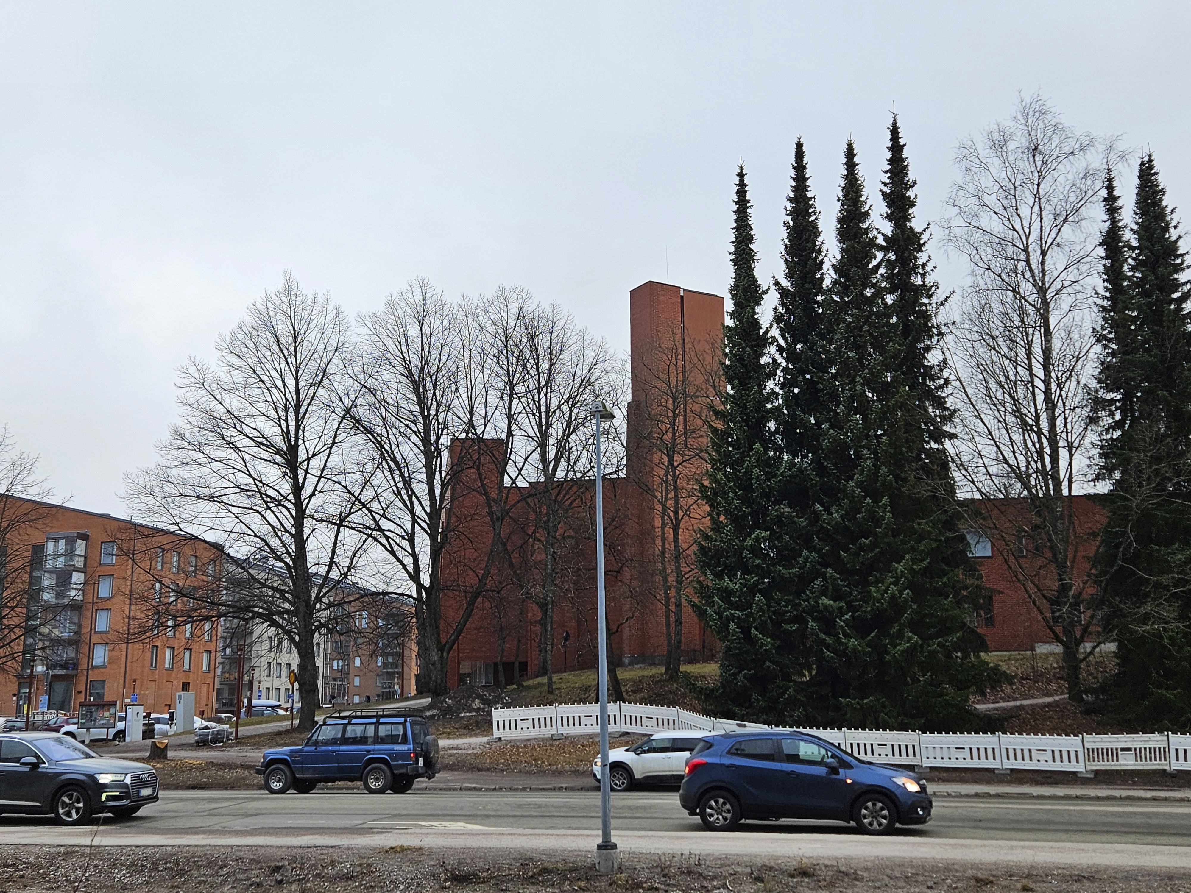 En stor kyrka i rödtegel och biltrfaik framför den på gatan.