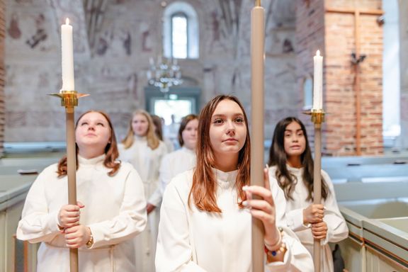 Unga konfirmandflickor i vita albor bär kors och ljus i procession.