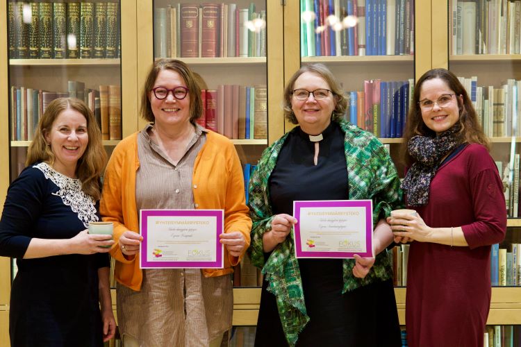 Fyra kvinnor står leende framför en bokhylla och håller upp prisdiplom.