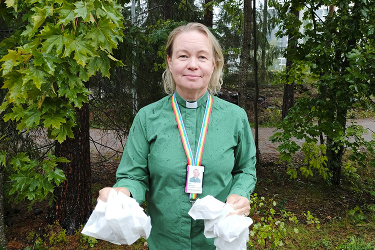 En kvinnlig diakon står utomhus i grönska och håller i sina bägge händer små vita påsar.