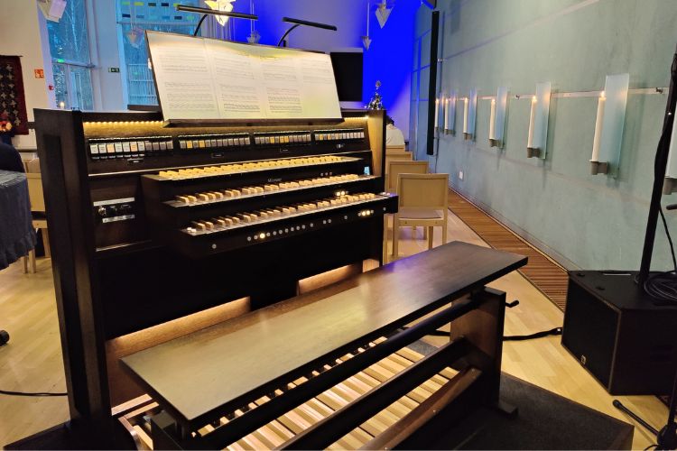 En orgel i svart står i ett upplyst utrymme.