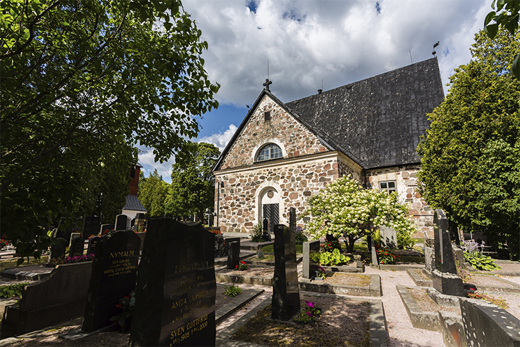Esbo domkyrka som är en gråstenskyrka fotograferad i lummig grönska.