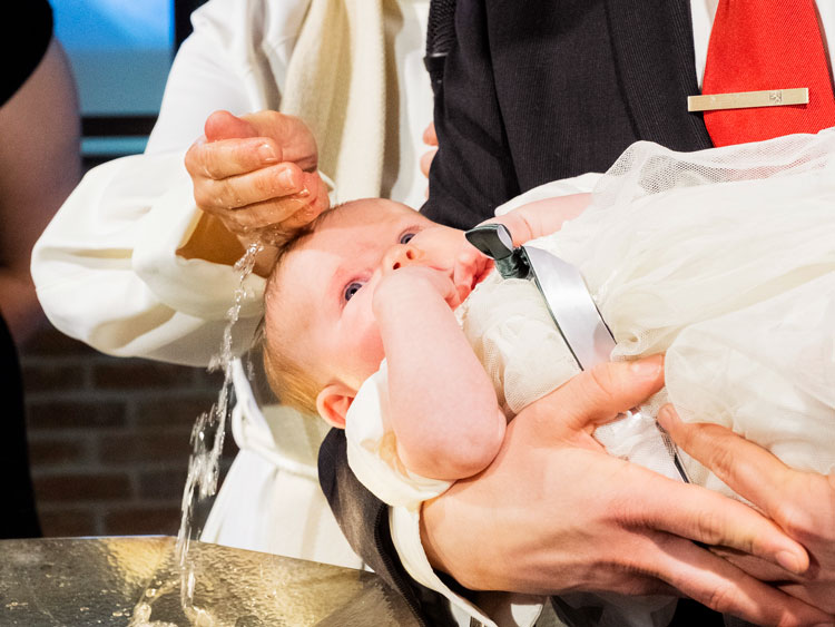 Ett barn döps vid dopfunten.