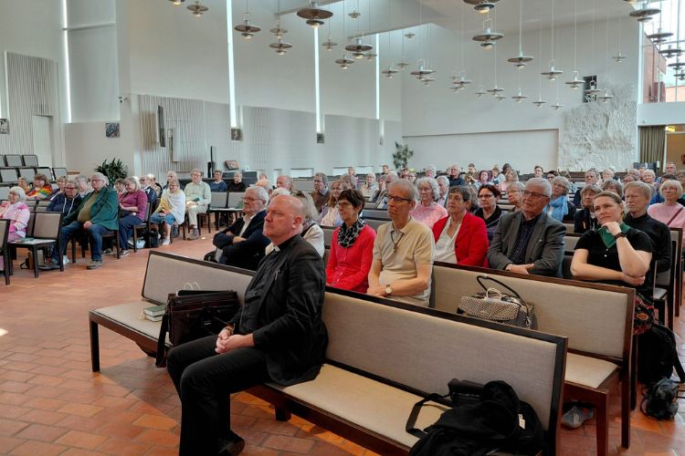 Många människor sitter i kyrkbänkarna i Olars kyrka.