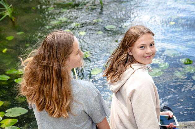 Två flickor med ljust långt hår sitter vid vatten.