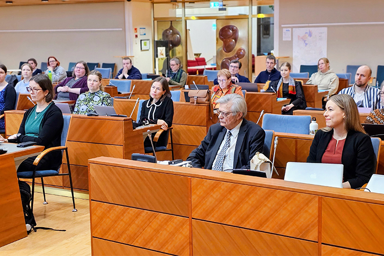 Knappt tjugo personer sitter i en sal som används för fullmäktigemöten.