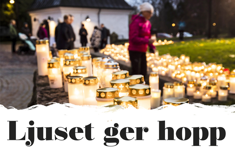 Tända gravljus på muren till Esbo domkyrka och i bakgrunden en kvinna som tänder ett ljus och övriga männis...