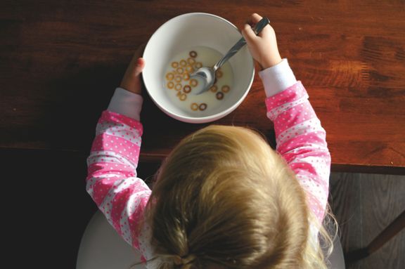 Ett litet barn sitter med en skål med flingor framför sig.
