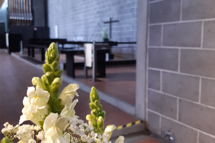 Vita blommor i förgrunden och i bakgrunden syns grått tegel och altaret med korset i svart i Hagalunds kyrka.