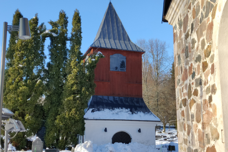 Esbo domkyrkas rödmålade klockstapel i vinterlandskap och sol.