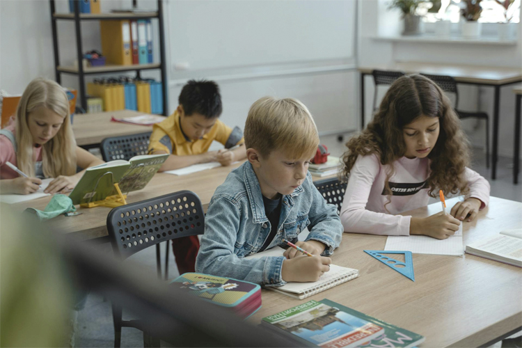 Fyra barn sitter vid sina pulpeter i ett klassrum.