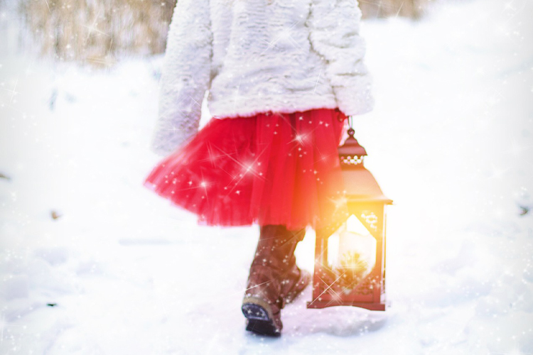 En flicka iklädd röd kjol och vit jacka går med en stallykta i snö.