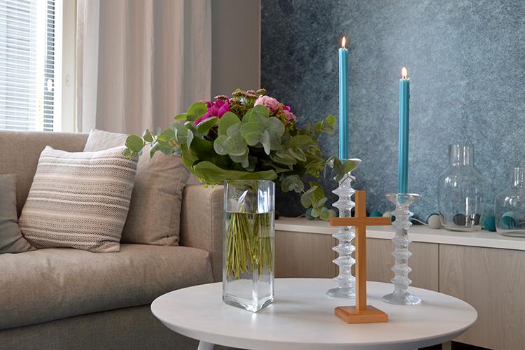 En soffa och ett bord med en vas med blommor, två tända ljus och ett kors.