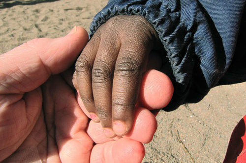 En vuxen som håller i ett mörkhyat barns hand.