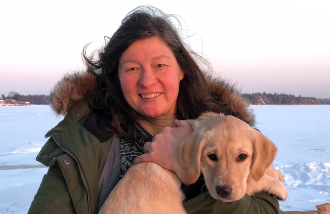 En kvinna med en hund i famnen mot bakgrunden av en snöig strand.