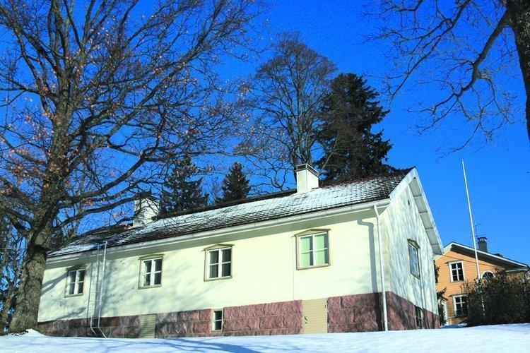 Ett vitt trähus med två skorstenar fotat på vintern med blå himmel och snötäckt mark.