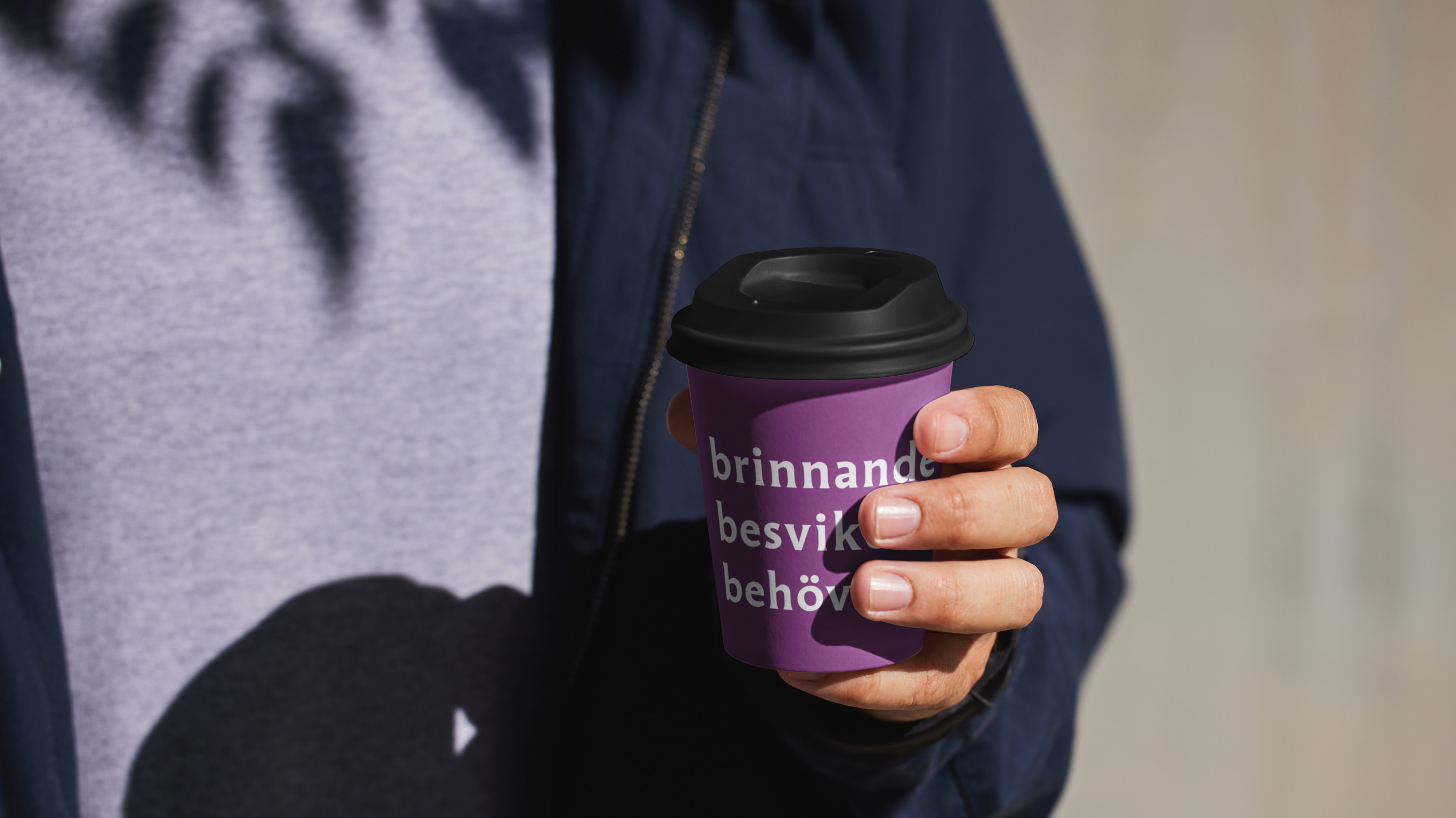 En hand med take away -kaffekopp med vallogo